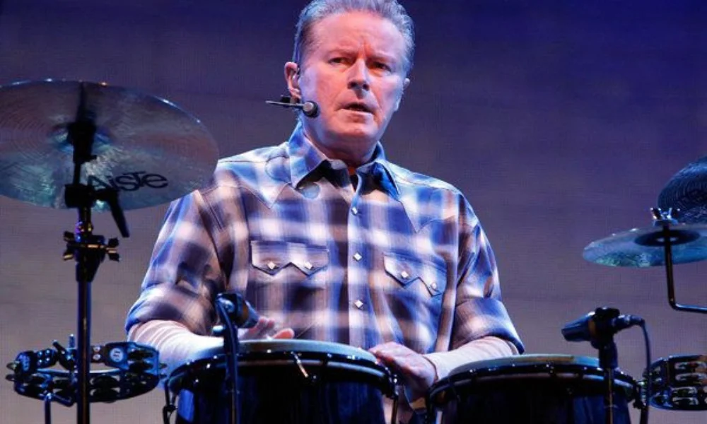A man in a plaid shirt plays drums on stage-don henley net worth