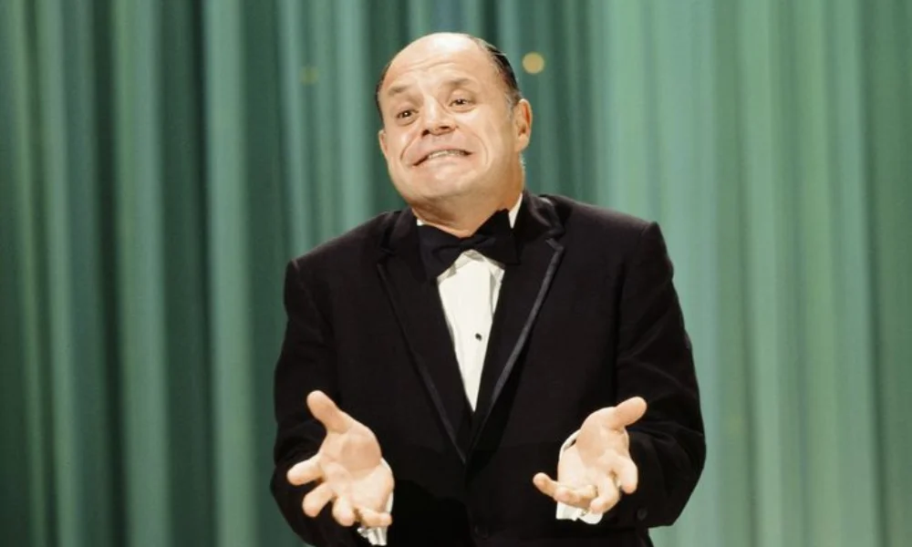 A man in a tuxedo performs on stage against a green curtain-don rickles net worth