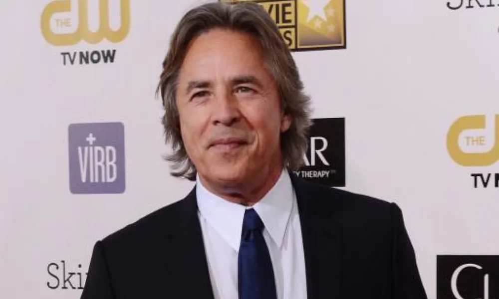 A man with gray hair, wearing a black suit and blue tie