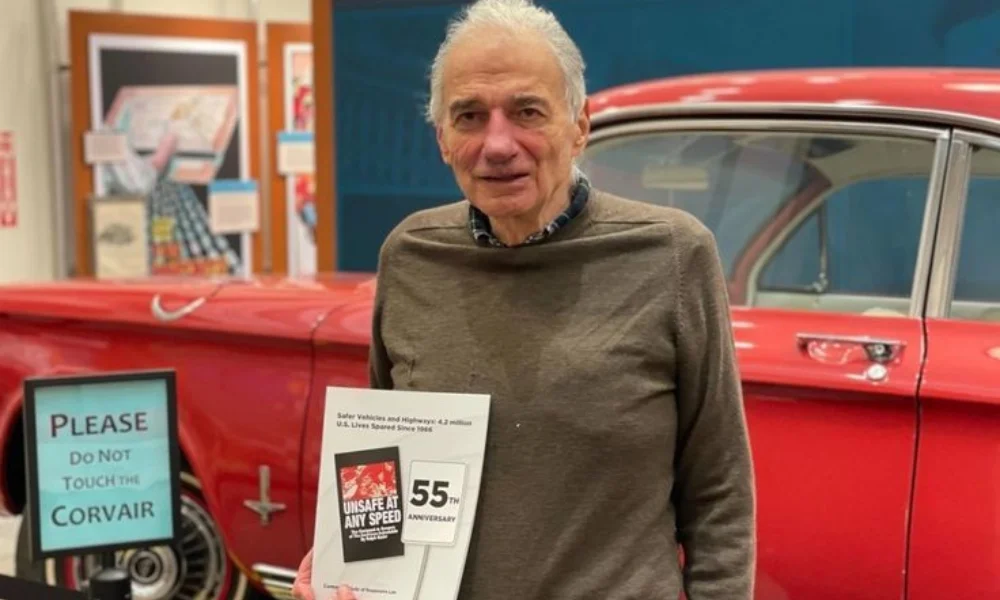 A man stands in front of a red vintage car,