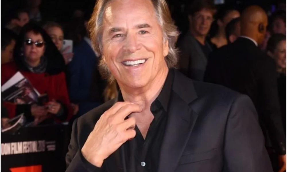 A smiling man in a black suit poses on a red carpet
