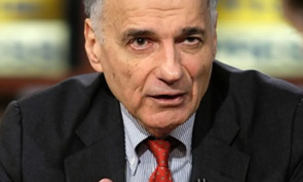 Elderly man in a suit and red tie speaks seriously