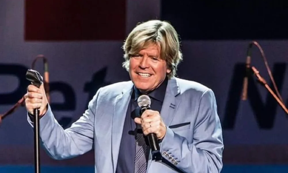 Man with medium-length blond hair in a light blue suit sings