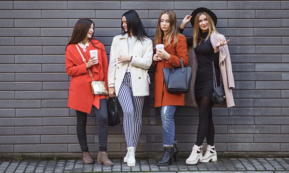Four stylish women stand against a gray brick wall-trending outfits for women