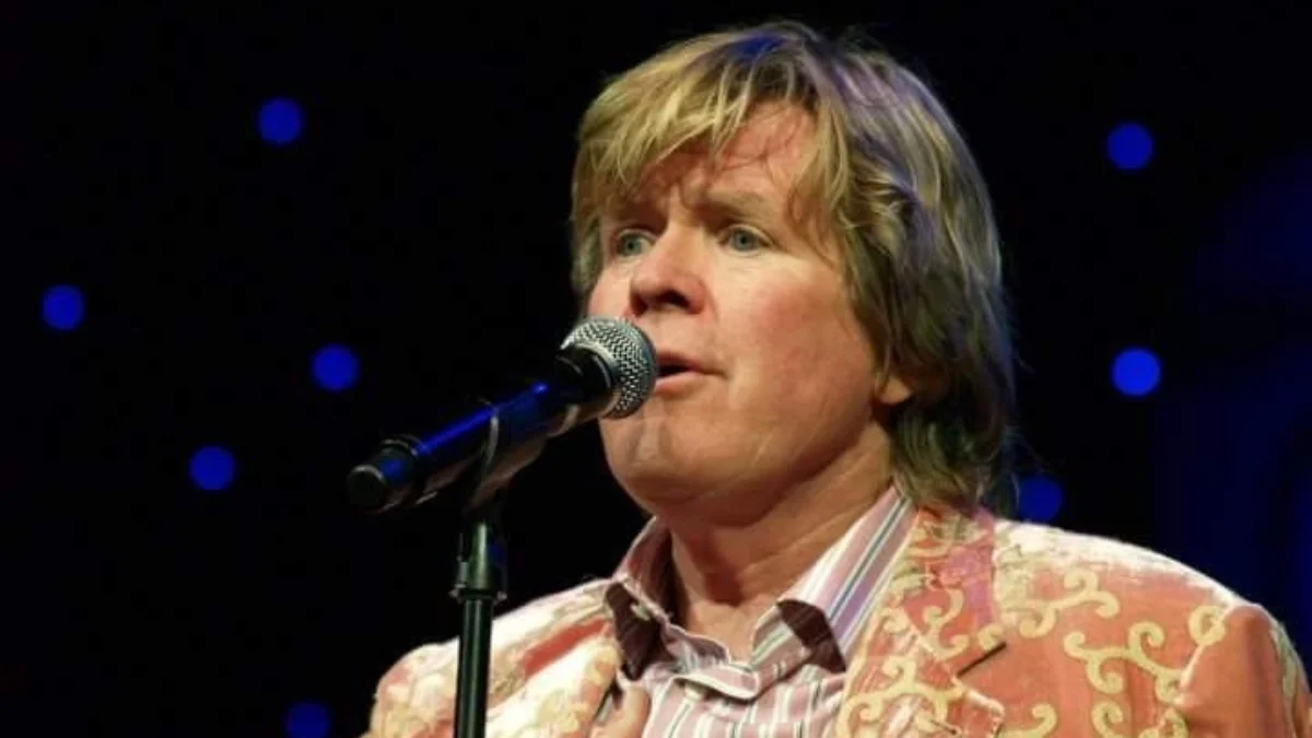 A person with medium-length hair sings into a microphone on stage
