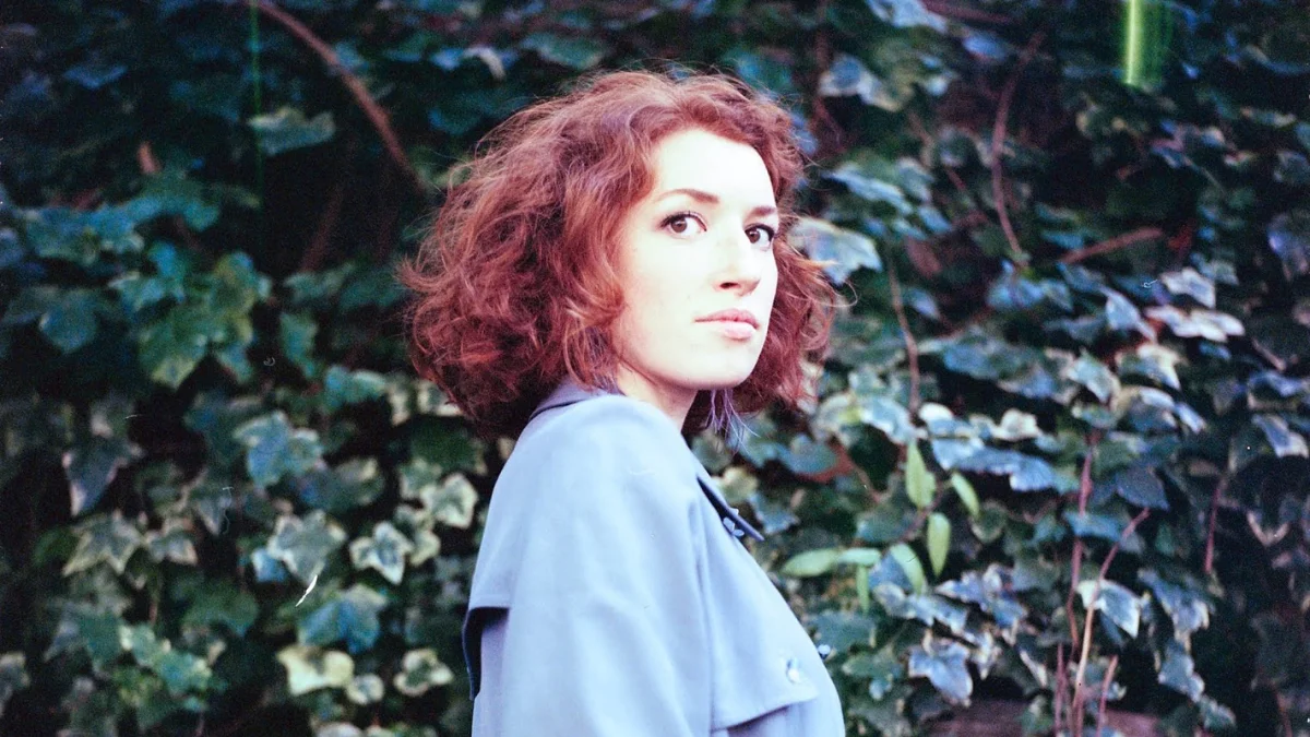 A woman with curly, auburn hair stands